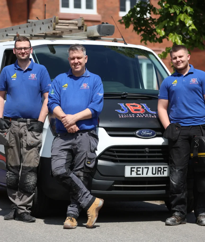 Three men wearing blue shirts and work pants stand in front of a white JBL Julian Bland Heating and Plumbing company van and a ladder on top, ready for their next home project.